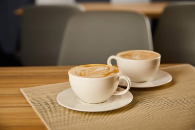 selective focus of creamy cappuccino in white cups on table  clipart