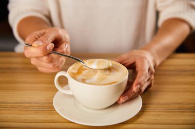 cropped view of woman holding spoon with cappuccino foam clipart