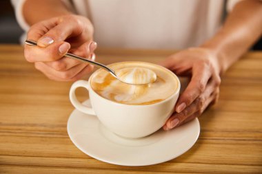 selective focus of woman holding spoon with cappuccino foam  clipart