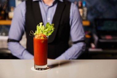 Barmen, Bloody Mary kokteylinin yanında kereviz ve camdaki karideslerle görülmüş. 