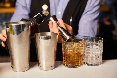 Barmen içki bardaklarının yanında içki şişesi tutuyor. 