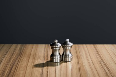metal salt and pepper shakers on wooden table isolated on black clipart