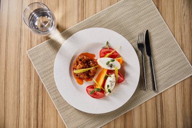 Patlıcan havyarlı ve domatesli lezzetli restoran yemekleri ahşap masa üzerinde su ve çatal bıçakla servis edilir.