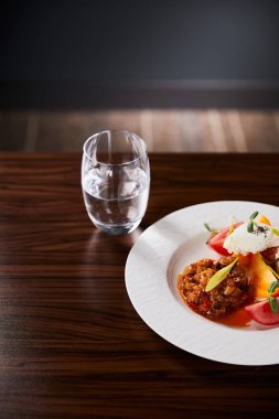 Patlıcan havyarlı ve domatesli lezzetli restoran yemekleri ahşap masada servis ediliyor ve siyah arka planda su var.