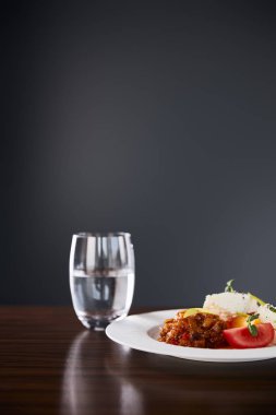 Patlıcan havyarlı ve domatesli lezzetli restoran yemekleri ahşap masada servis ediliyor ve siyah arka planda su var.