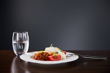 Patlıcan havyarlı ve domatesli lezzetli restoran yemekleri ahşap masada servis ediliyor. Siyah arka planda su ve çatal bıçak takımı var.