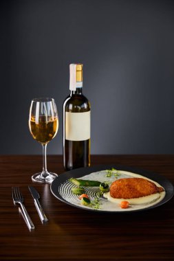 Lezzetli tavuk kiev ve patates püresi tabakta çatal bıçak takımının yanında ve siyah arka planda beyaz şarap servis ediliyor.
