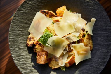Güneş ışığında tabakta servis edilen parmesan dilimli lezzetli Sezar salatasının yakın görüntüsü.