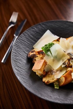 Parmesan dilimli lezzetli Sezar salatasının seçici odak noktası ahşap masada çatal bıçakla servis edilen tabakta.