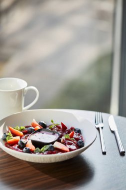 Geleneksel Ukraynalı varenky. Beyaz tabakta servis edilen böğürtlenler, çatal bıçak ve fincanın yanında servis edilen sos. Restorandaki ahşap masada.