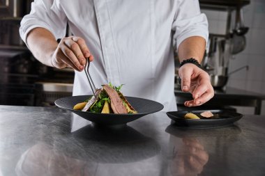 partial view of chef making dish with arugula, meat and potato at kitchen in restaurant clipart