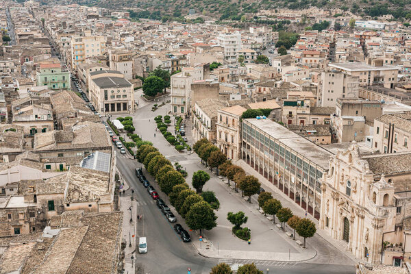 SCICLI, ITALY - OCTOBER 3, 2019: old city with small houses and san michele arcangelo church near green trees on streets in sicily 