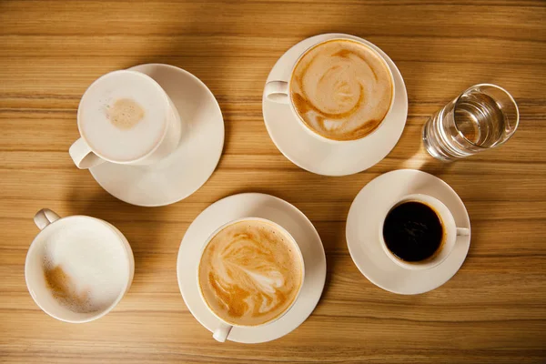 Vista Superior Platillos Con Tazas Café Diferentes Cerca Vaso Agua — Foto de Stock