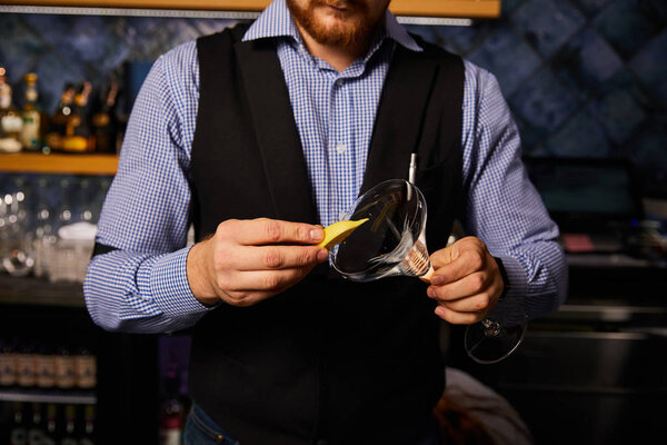 cropped view of bearded barman holding sliced lemon near margarita glass 
