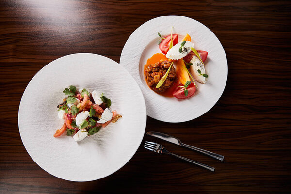 top view of delicious restaurant dish with eggplant caviar and tomatoes and salad on wooden table with fork and knife