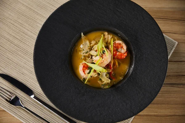 上图是用黑盘虾仁和餐具在餐巾纸上食用的美味餐厅汤 — 图库照片