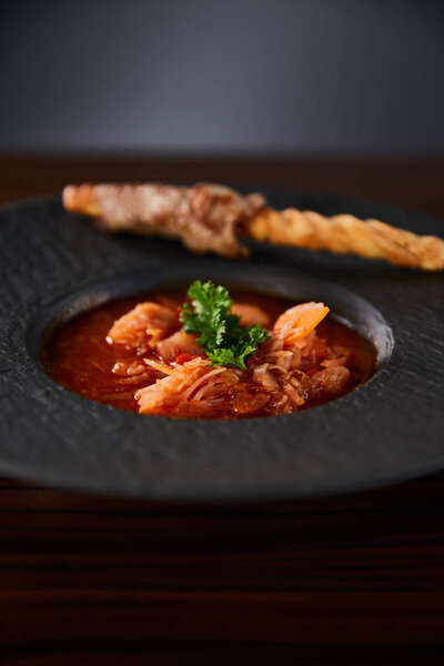 закрытый вид на традиционный украинский борщ, украшенный петрушкой в черной тарелке
