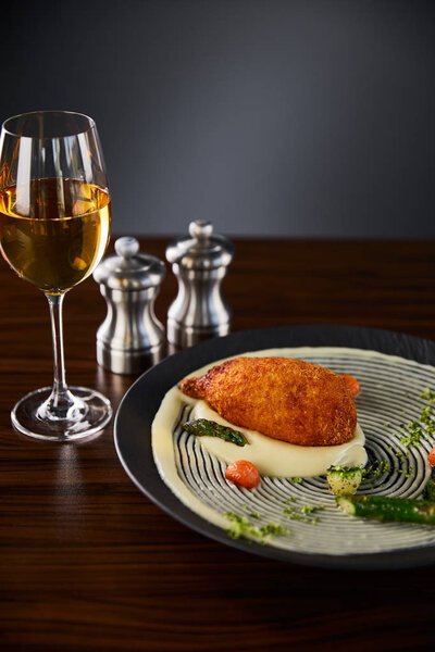 вкусный куриный киев и картофельное пюре подается на тарелке возле белого вина на черном фоне
