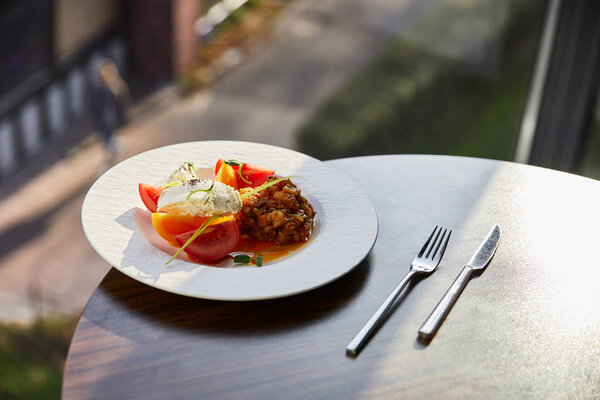 delicious eggplant caviar with tomato and butter served in restaurant on wooden table with cutlery in sunlight