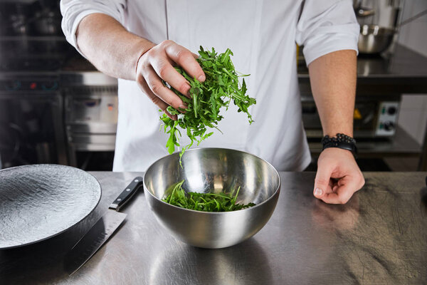 cropped view of chef cooking salad with arugula at kitchen in restaurant
