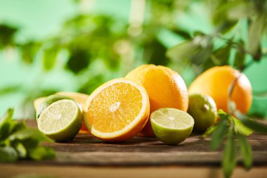 selective focus of cut, whole oranges and limes on wooden surface  clipart