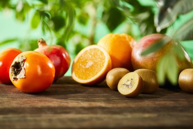 Tahta masa üzerinde seçici kivi, portakal, nar, mango ve hurma odağı. 