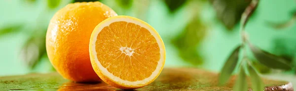 panoramic shot of cut and whole oranges on wooden cutting board