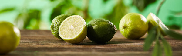 panoramic shot of cut and whole limes on wooden surface 