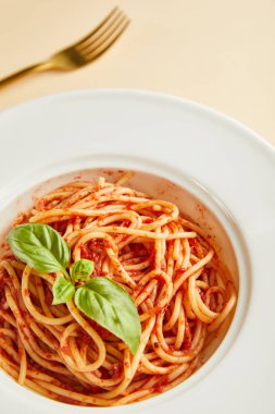 Domates soslu leziz spagetti ve sarı arka planda çatalın yanında fesleğen.