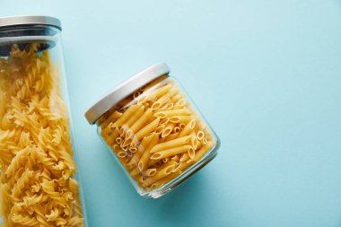 Üst görünüm ham penne ve fusilli kavanozlarda mavi arkaplan üzerinde kopyalama alanı ile