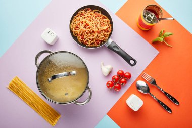 Domates soslu leziz spagetti ve kırmızı, mavi ve mor arka planda pişirme aletleri.