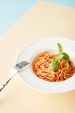 Mavi ve sarı arka planda çatalın yanında domates soslu lezzetli spagetti.