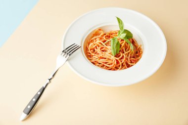 Mavi ve sarı arka planda çatalın yanında domates soslu spagetti.