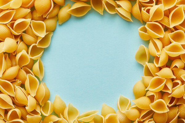 round frame of raw Conchiglie on blue background with copy space