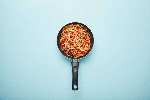 top view of delicious spaghetti with tomato sauce in frying pan on blue background