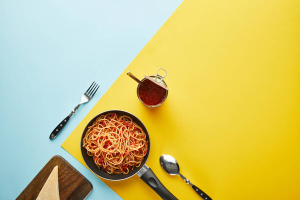flat lay with delicious spaghetti with tomato sauce with parmesan on blue and yellow background