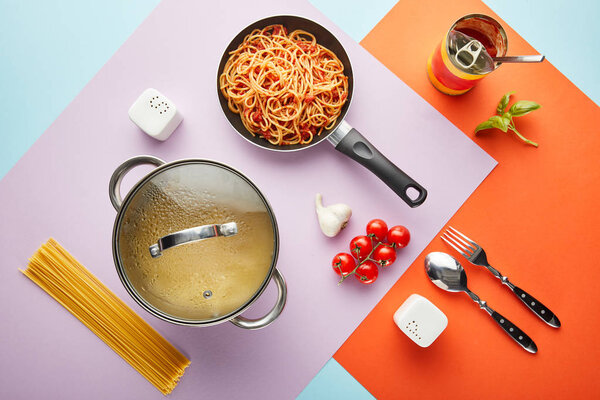 flat lay with delicious spaghetti with tomato sauce ingredients and cooking utensils on red, blue and violet background