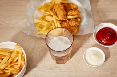 Bir bardak bira, patates kızartmalı tavuk nugget ketçap ve ahşap masada mayonez.