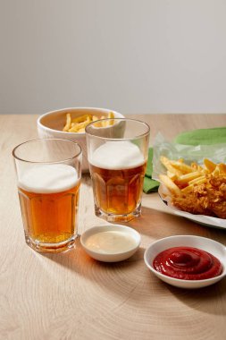 Bir bardak bira, patates kızartmalı tavuk nugget ketçap ve mayonez tahta masa üzerinde gri arka planda.