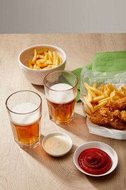 Bir bardak bira, patates kızartmalı tavuk nugget ketçap ve mayonez tahta masa üzerinde gri arka planda.