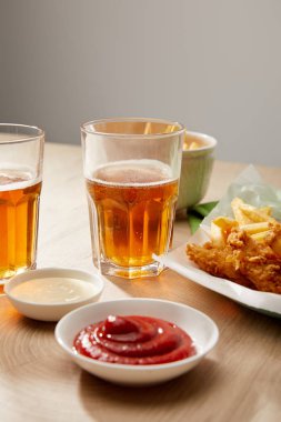 Bir bardak bira, patates kızartmalı tavuk nugget ketçap ve mayonez tahta masa üzerinde gri arka planda.