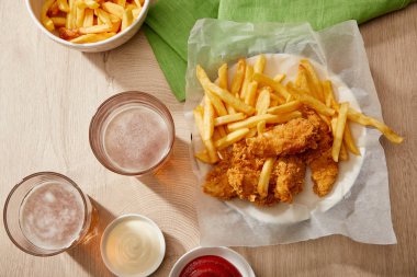 Bardakların üst görüntüsü, patates kızartmalı tavuk nugget, ketçap ve mayonez tahta masa üzerinde gri arka planda.
