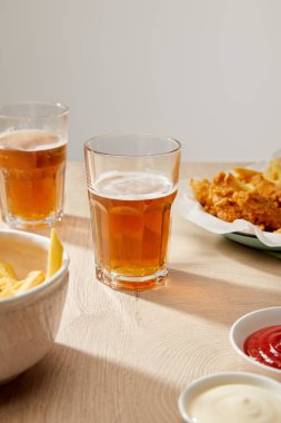 Bir bardak bira, patates kızartmalı tavuk nugget ketçap ve mayonez tahta masa üzerinde gri arka planda.