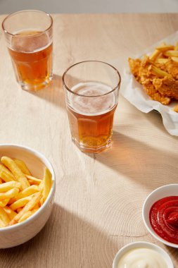 Bir bardak bira, patates kızartmalı tavuk nugget ketçap ve ahşap masada mayonez.