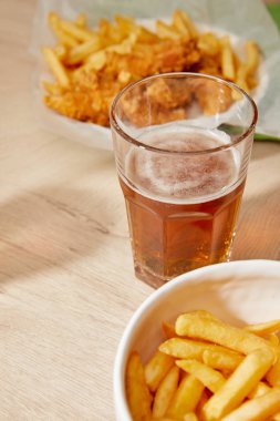 Bir bardak biranın seçici odağı, ahşap masada patates kızartmalı tavuk nugget.