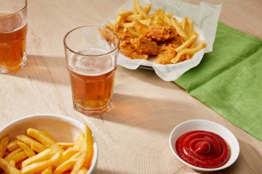 Bir bardak bira, patates kızartmalı tavuk nugget, ahşap masada ketçap.