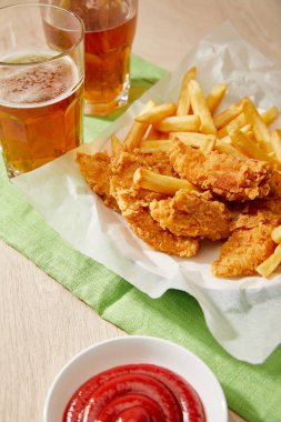Bir bardak bira, patates kızartmalı tavuk nugget, ahşap masada ketçap.