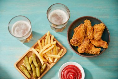 Lezzetli tavuk nugget, ketçap, patates kızartması ve turkuaz masa üzerinde bira bardaklarının yanında salatalık turşusu manzarası.