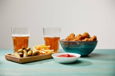 delicious chicken nuggets, ketchup, french fries and gherkins near glasses of beer on turquoise wooden table isolated on grey clipart