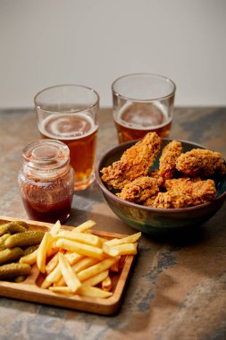 delicious chicken nuggets, french fries and gherkins near glasses of beer on stone surface isolated on grey clipart